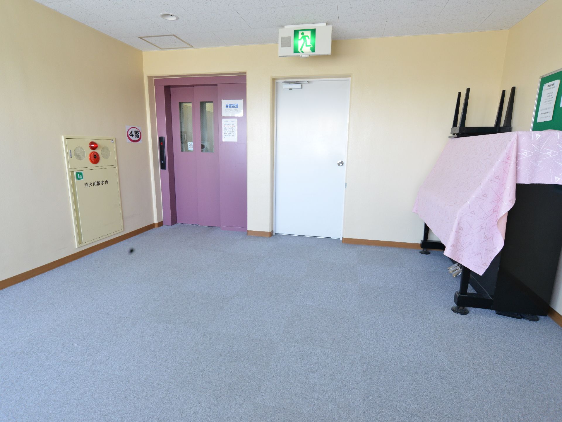 4階エレベーター前のゆったりしたスペース。壁際にはアプライトピアノが置かれている。隣にあるのは緊急時の避難用出口。