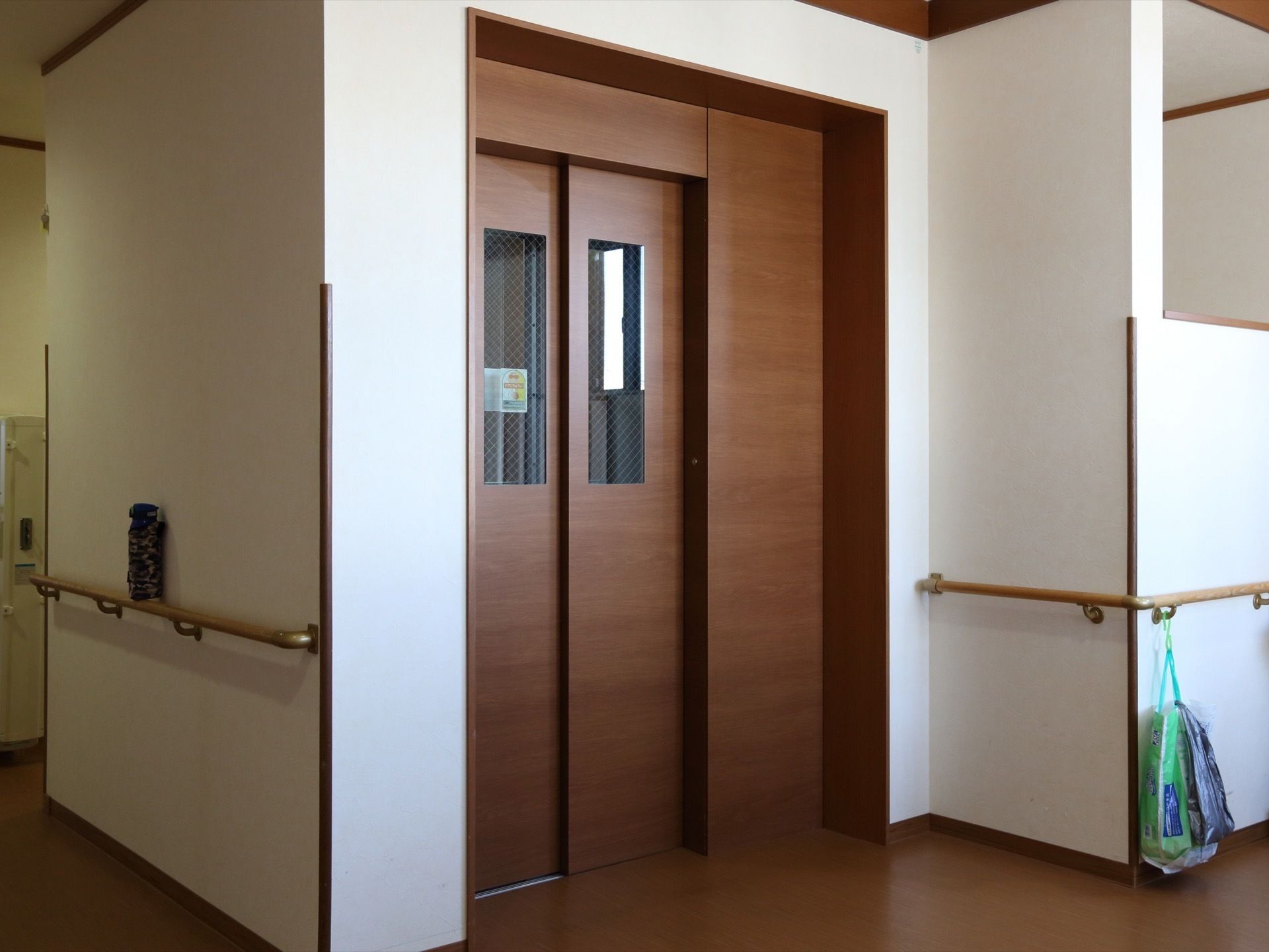 施設の中はエレベーターが設置されている。デザインはおしゃれな木目柄で高級感がある。壁伝いに手すりが続いて付けてある。