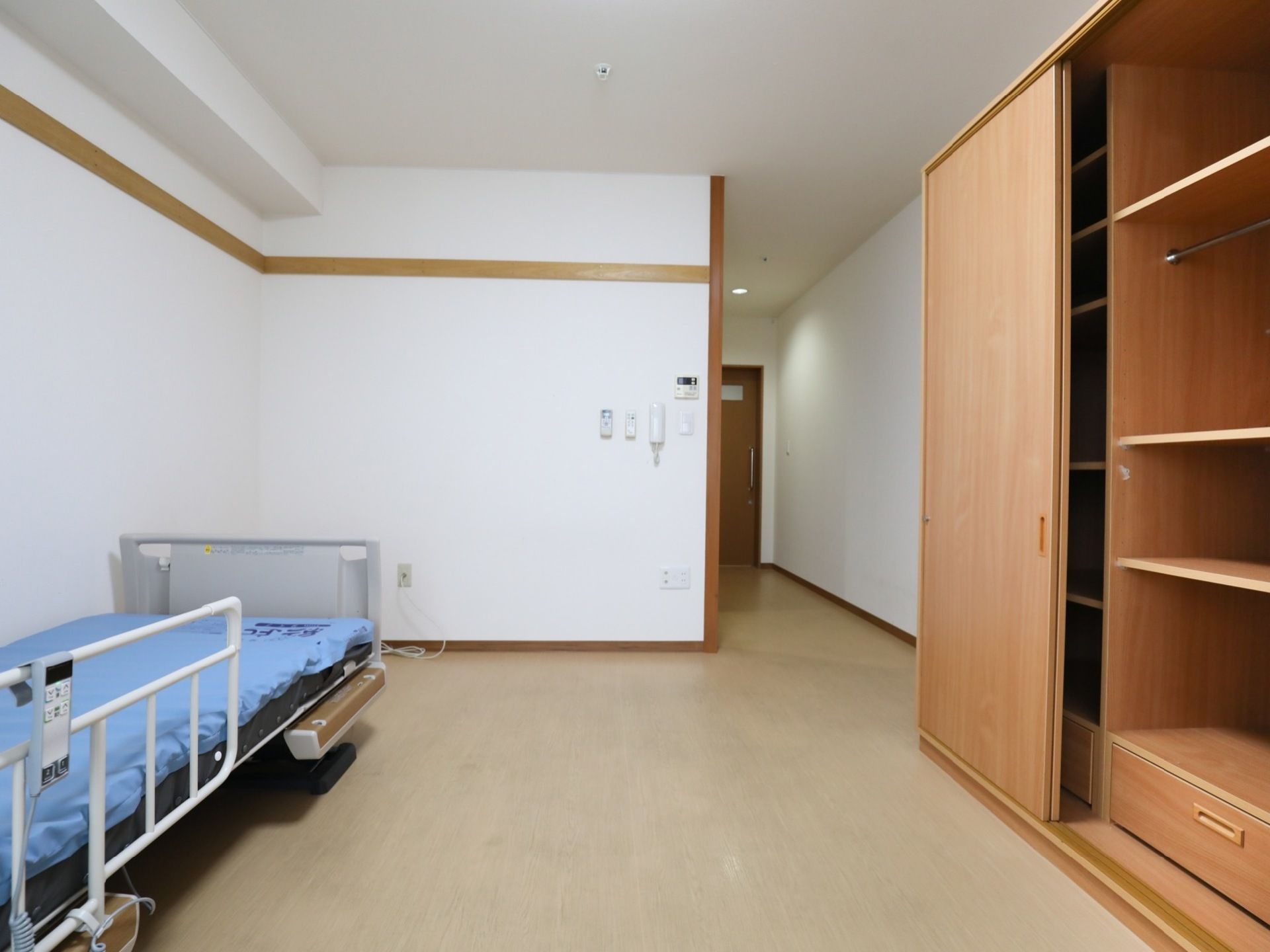 1人用居室の奥から入口の方向を見た様子である。介護ベッド、大きめの収納棚がある。収納棚は引き戸になっている。