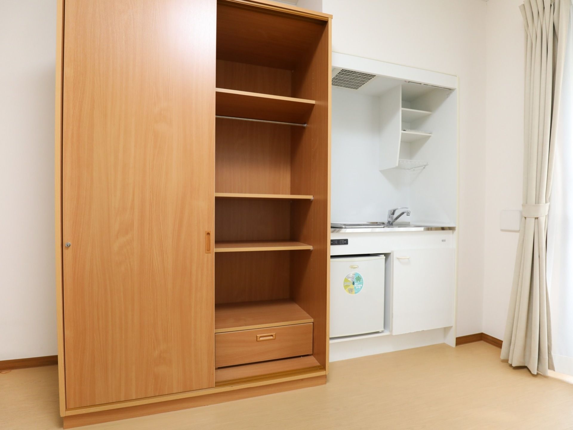 居室に備え付けの収納棚とキッチン。収納棚はスライド式の扉で、部屋を広く使用できる。キッチンにはそれぞれ小さな流し、コンロ、冷蔵庫、棚がある。
