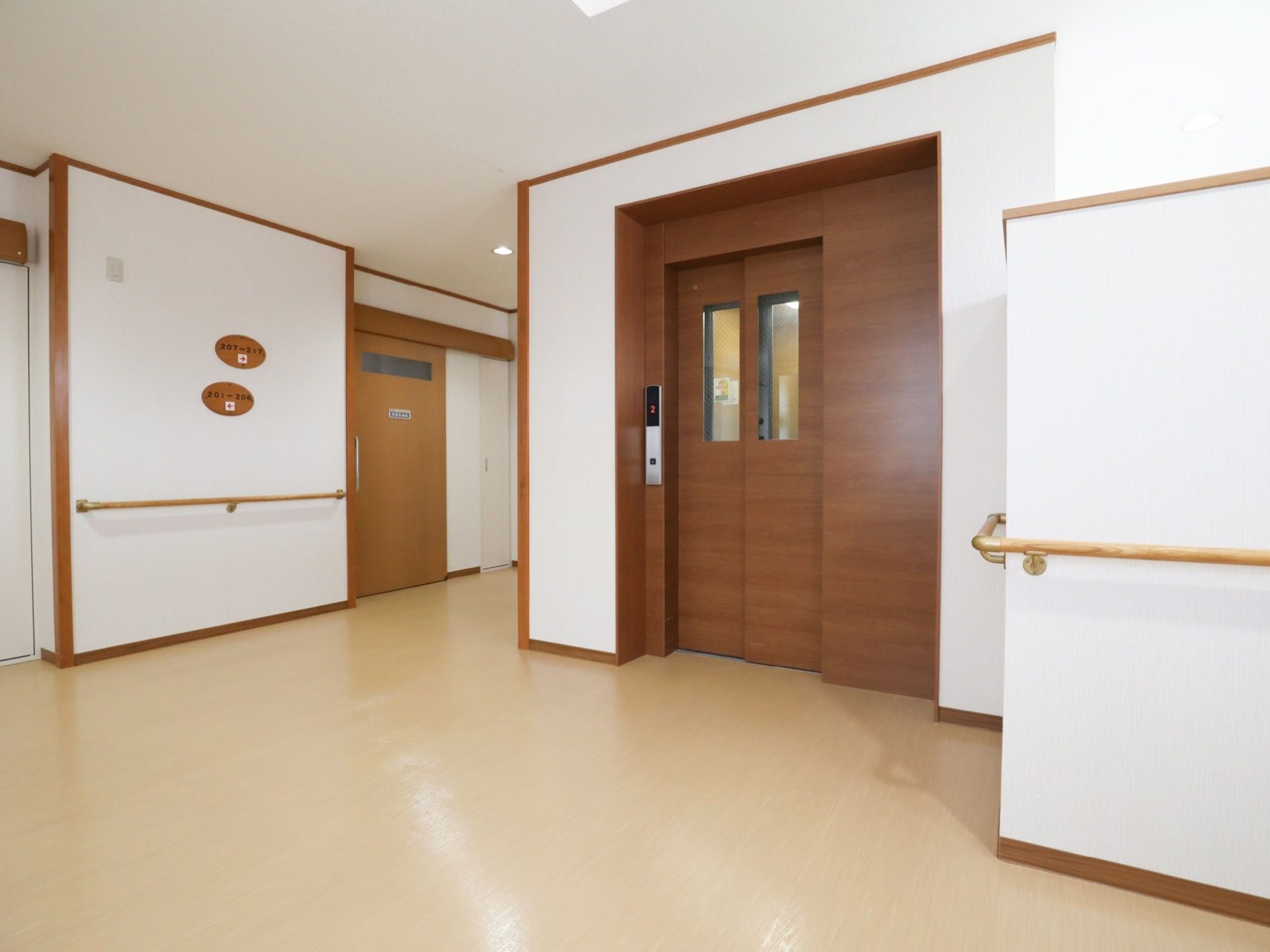 温かみのある木目調のエレベータードアの前に、広いスペースがある。周囲の壁には手すりが付けられている。