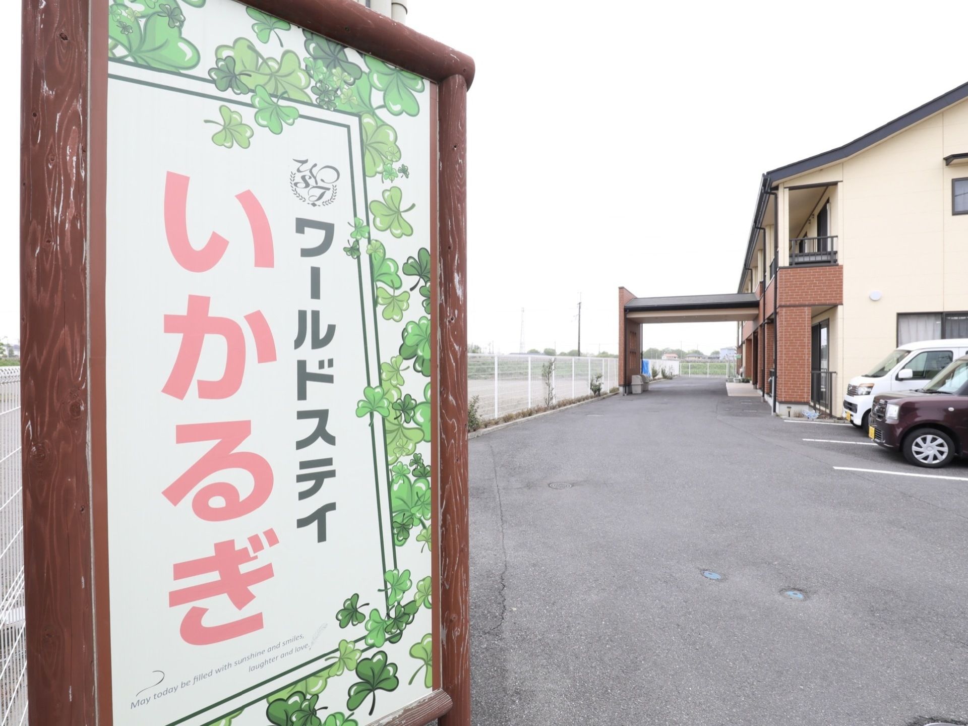 手前に施設名を表記した看板が立っている。広い敷地内に駐車スペースがある。奥には2階建ての施設建物が見えている。