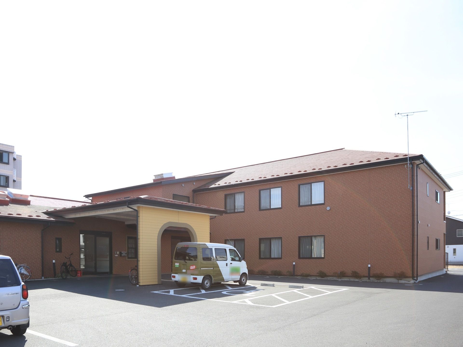 居住棟とは別に１階建ての建物があり、こちらに施設の入口がある。入口までの通路には屋根があり、駐車スペースも広い。