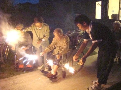 スタッフや他の入居者と一緒に花火を楽しむ、車椅子の女性