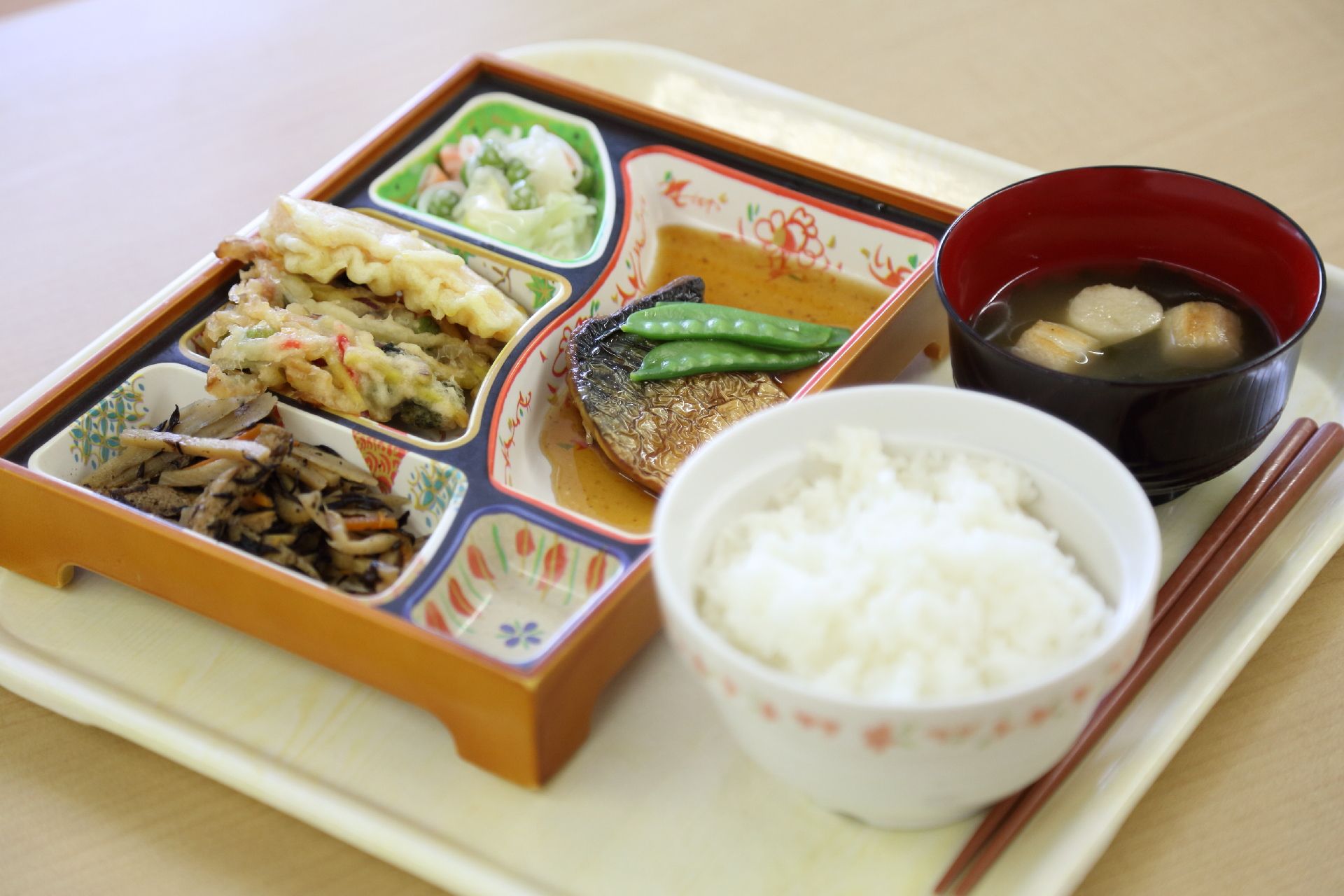ご飯とお味噌汁、天ぷらや煮物、魚の煮つけなどが並んでいるトレー