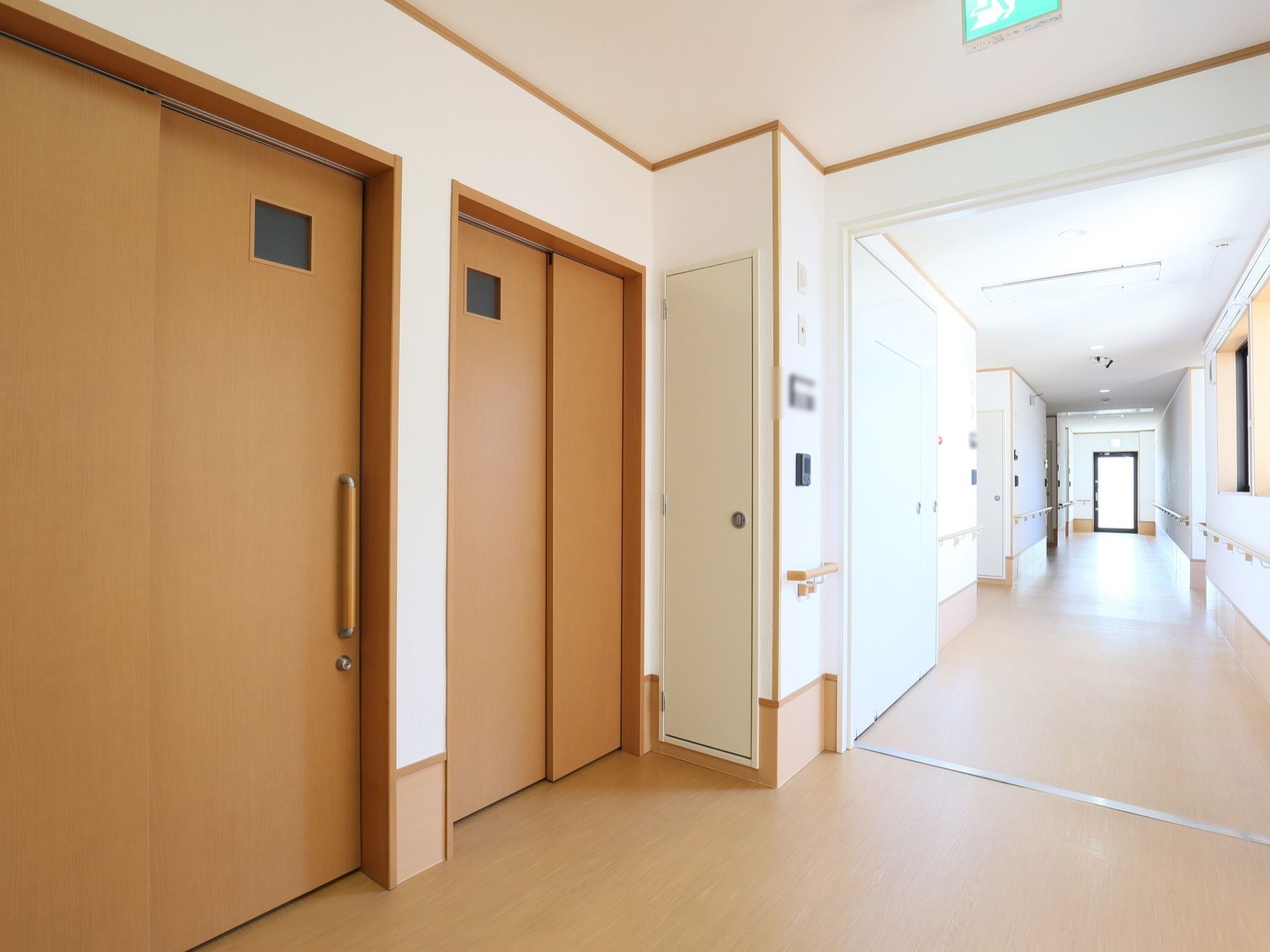 右奥に向かって廊下が伸び、突き当たりには外へ出られる非常扉がある。左手前には引き戸が２枚並んでいる。
