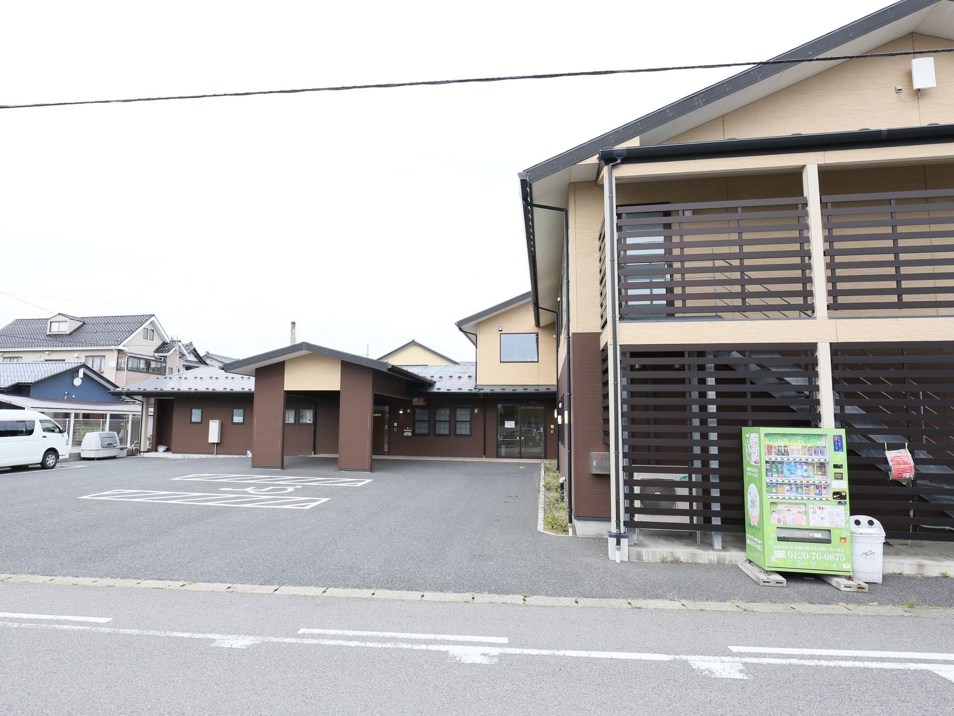 １階部分が茶色、２階部分がクリーム色に塗り分けられた施設で、外階段には黒い目隠しの柵が取り付けられている。