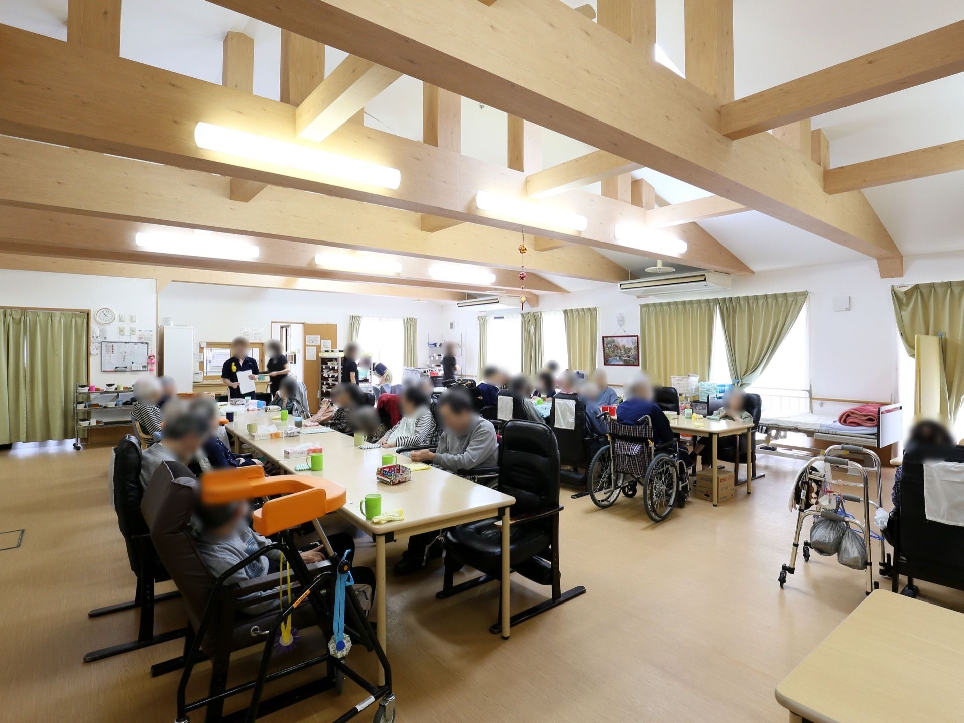 食堂の中央にテーブルが縦に２列に並べられ、入居者様が集まって食事を取れるようになっている。窓際には休憩用のベッドが設置されている。