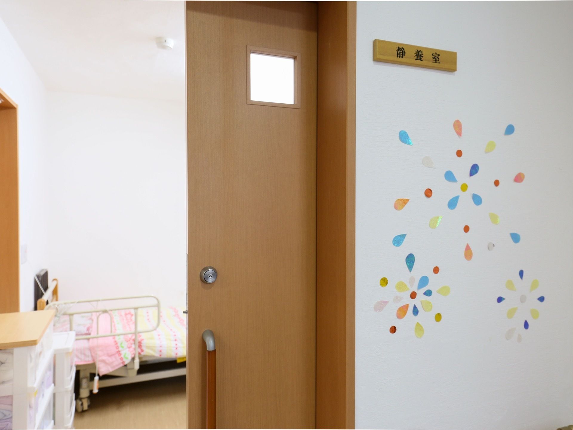 お部屋のドアは、木目調のスライド式である。その横側の壁に静養室のプレートを掲げ、お花をイメージする切り絵も貼られている。