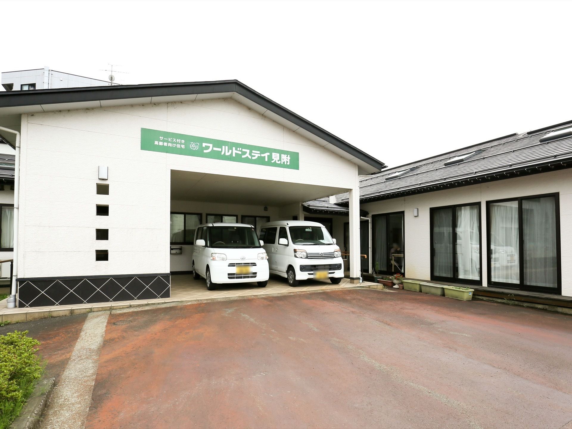 三角屋根が特徴的な外観である。車が２台停められている。外壁には施設名を明記したグリーンの看板を掲げている。