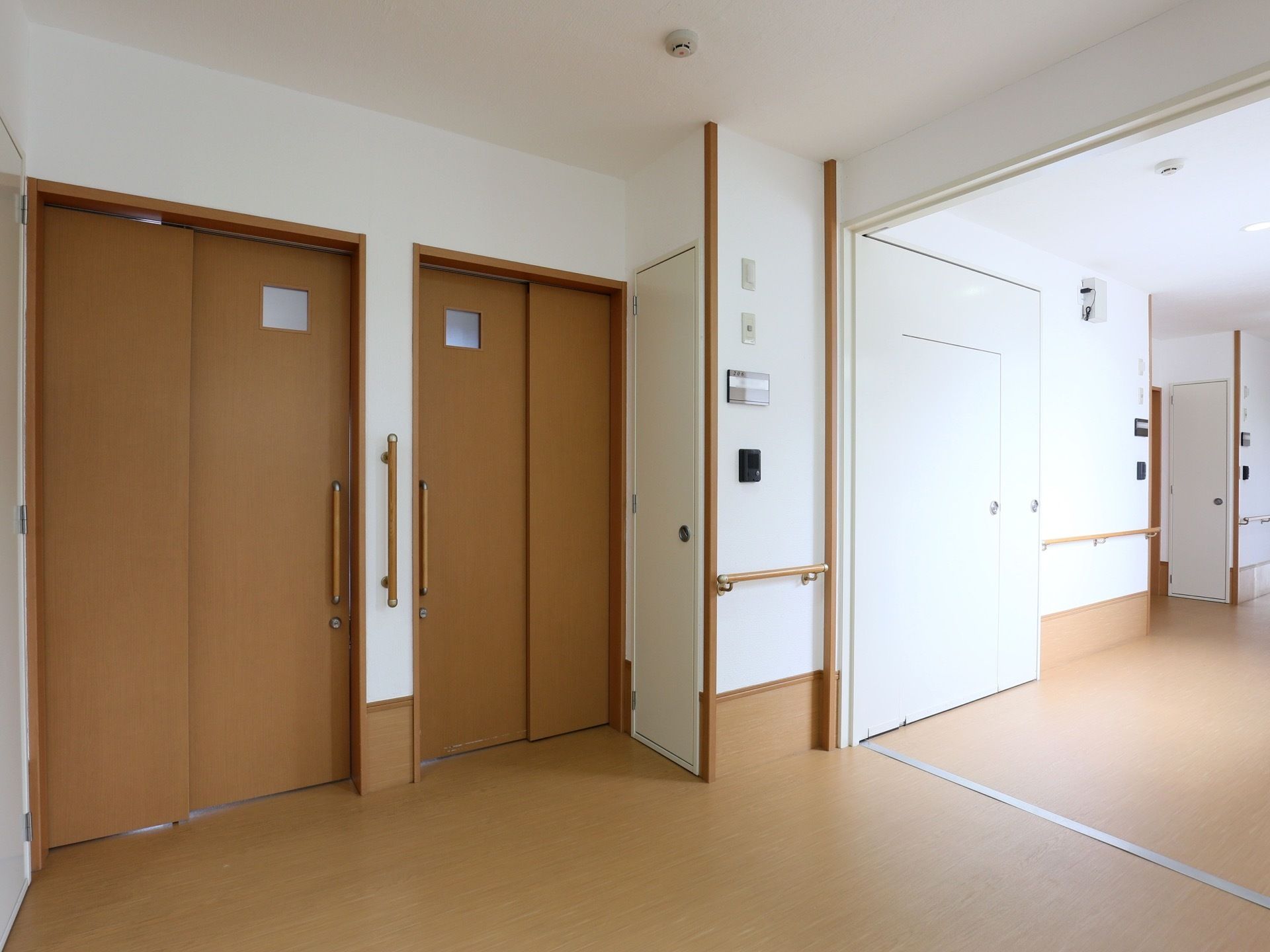 茶色のスライド式のドアがあり大きな取っ手が取り付けられている。壁に部屋番号が書かれたプレートとインターフォンが設置されている。