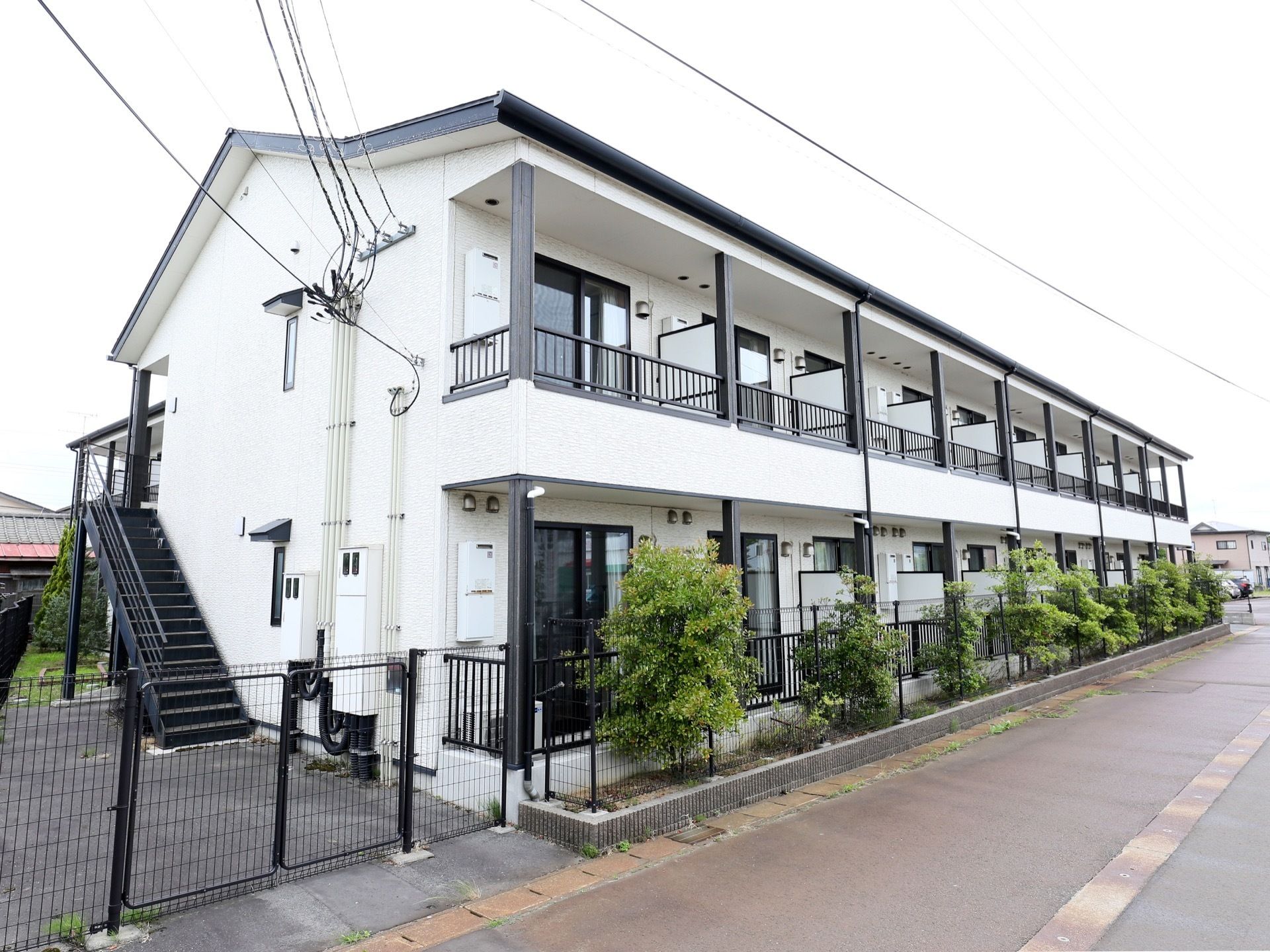建物の外側に黒いフェンスが設置されており、フェンスに沿うようにさまざまな高さの樹木が植えられている。