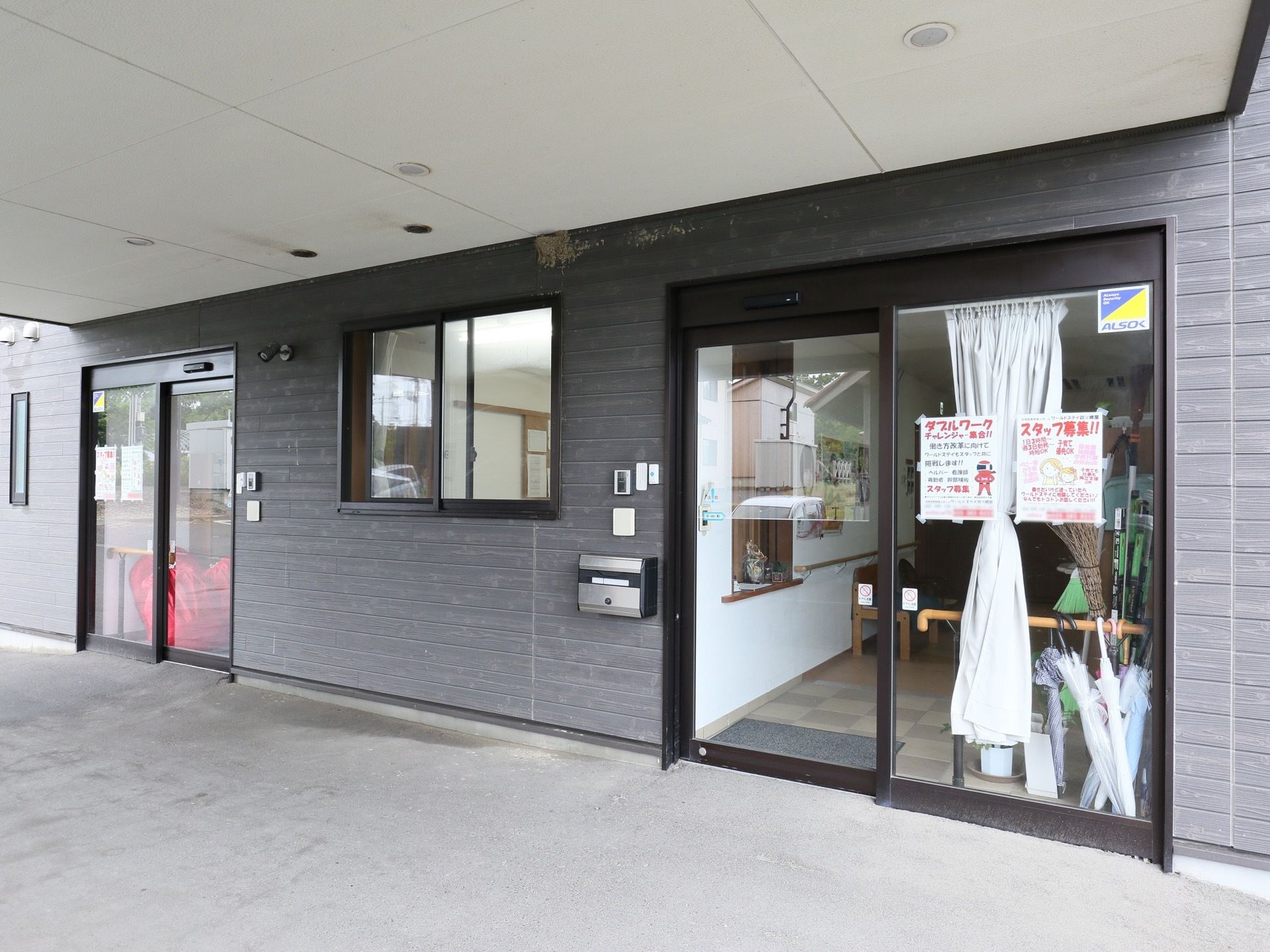 施設はダークグレーの外壁で、入口はガラス張りの自動ドアが設置されている。壁には、インターフォンやポストも取りつけられている。