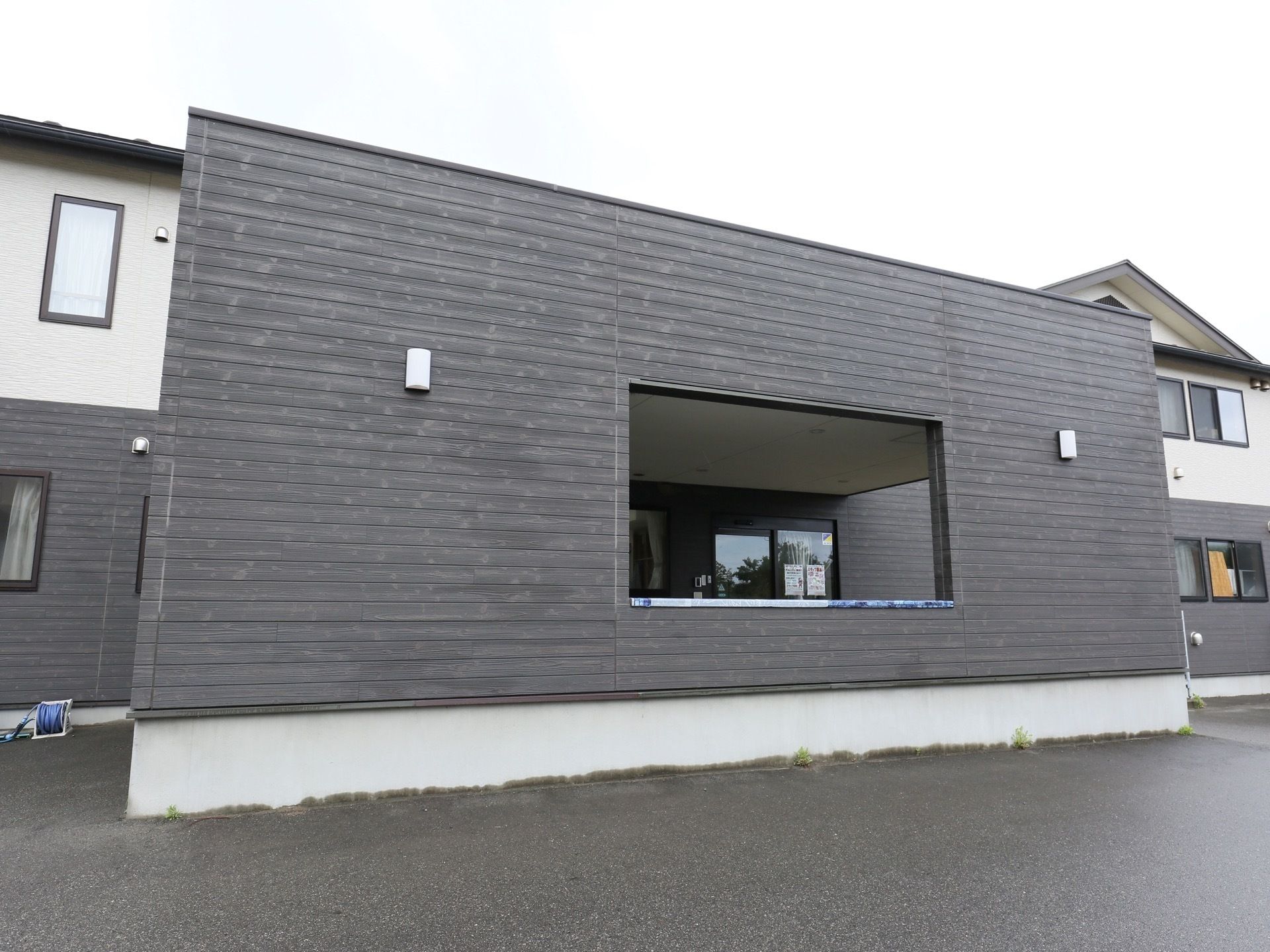 施設はダークグレーとホワイトの外壁で、2階建ての建物となっている。玄関は、屋根と壁で囲われた広いスペースが確保されている。
