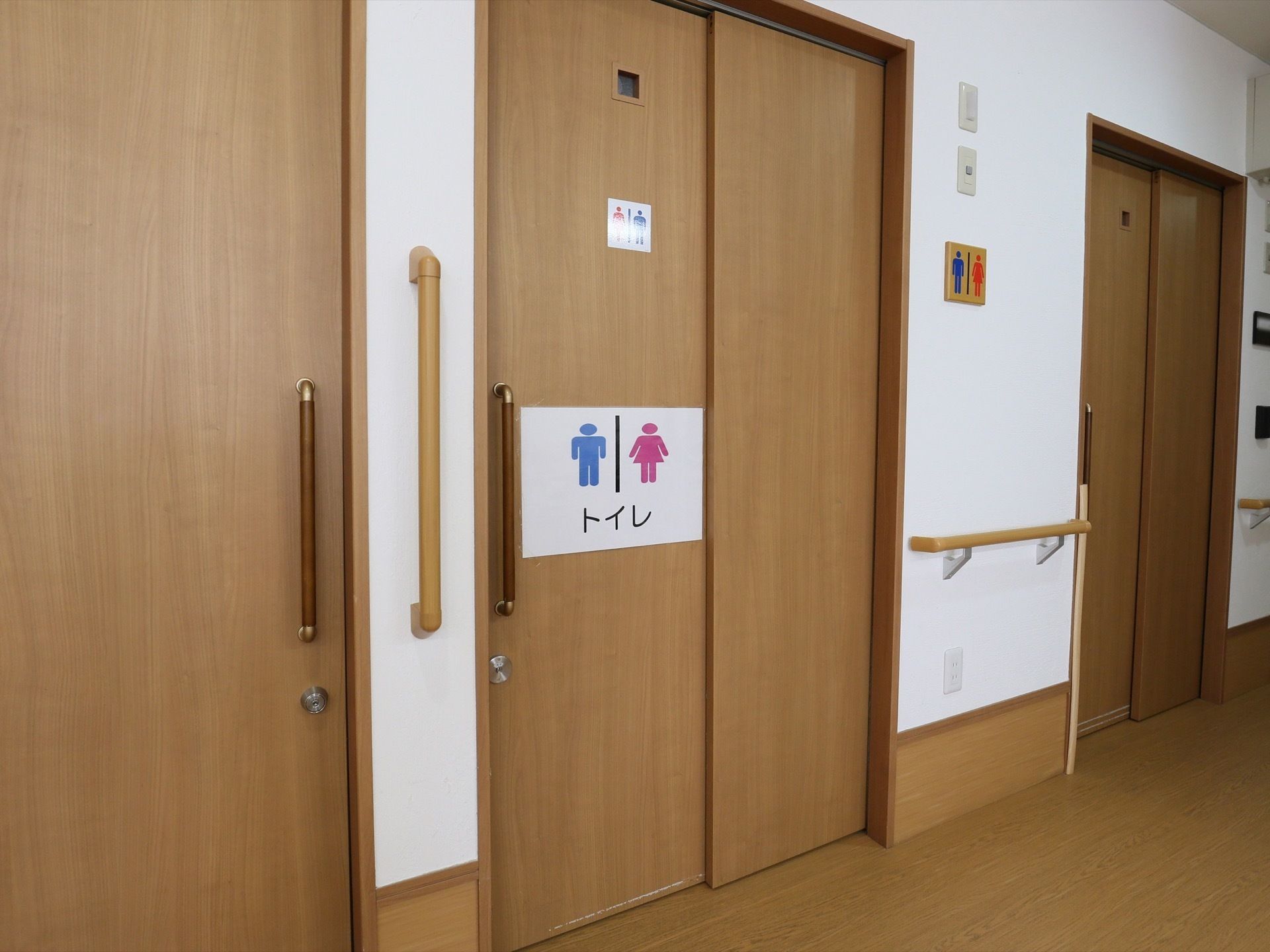 廊下はフローリングの床で、一角にはトイレが設けられている。壁には縦向きや横向きの手すりが取りつけられている。