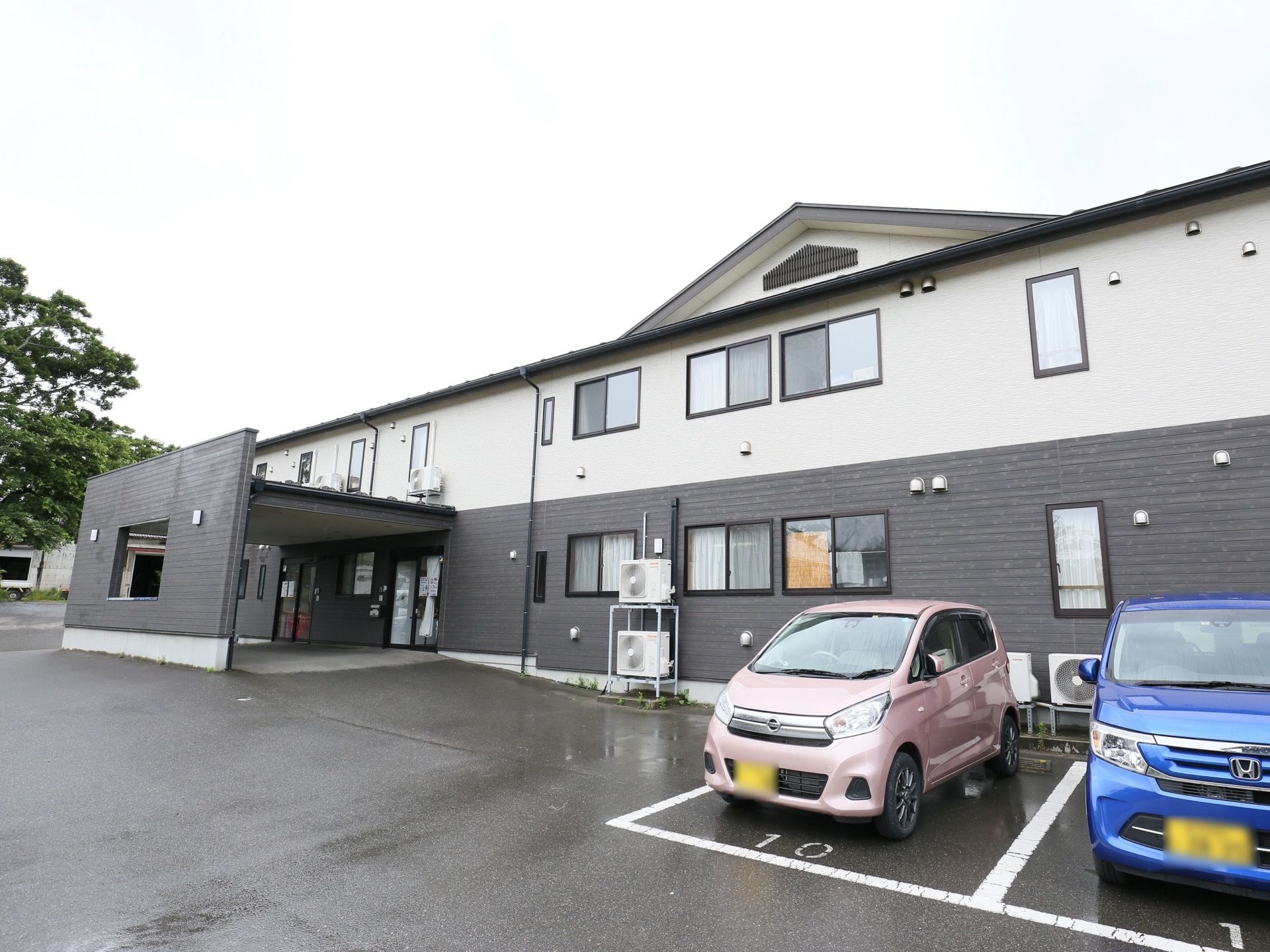 施設の敷地は広く、正面には番号の書かれた駐車スペースが設けられている。玄関前には、大きな屋根も取りつけられている。