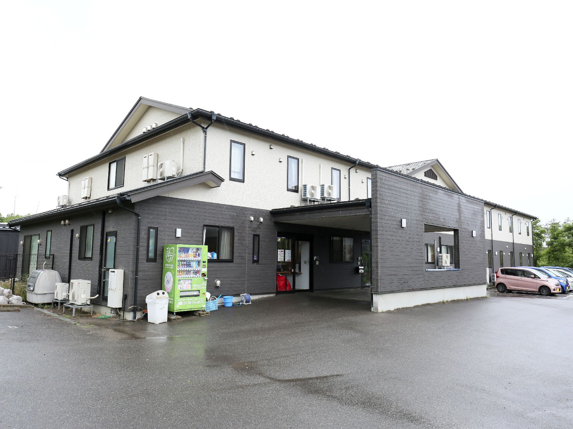 広い駐車場や自動販売機がある、戸建て住宅のような外観の建物