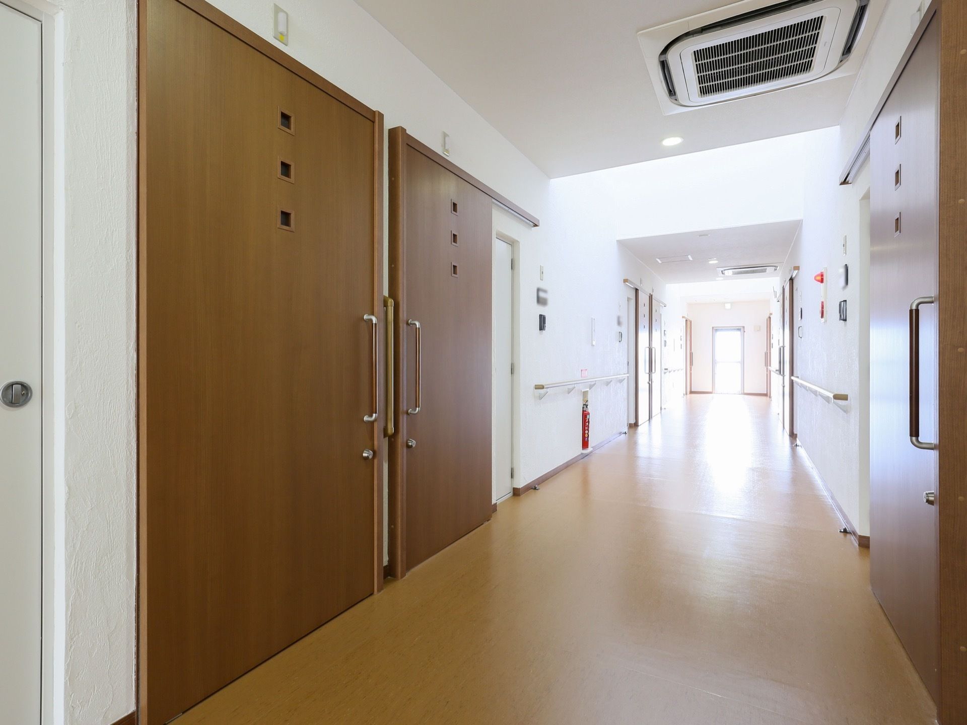 木目調デザインの引き戸は、大きなサイズである。各部屋のドア横には、表札パネルが付いている。天井には、空調がある。