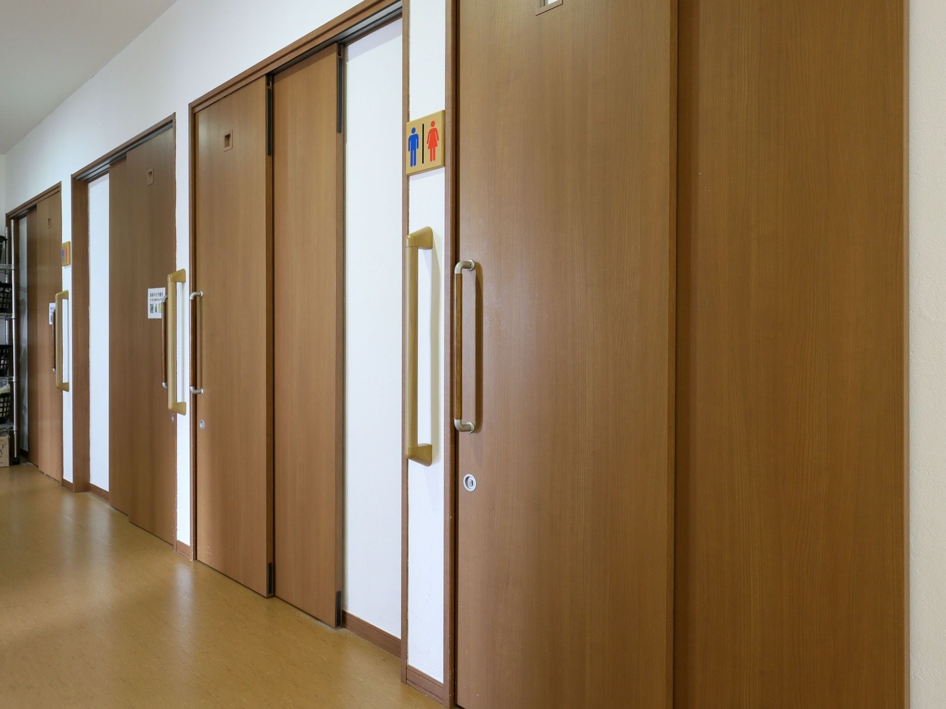 トイレのマークが描かれた木製の表示パネルが、白い壁に付いている。木目調デザインの引き戸には、シルバーの鍵穴がある。