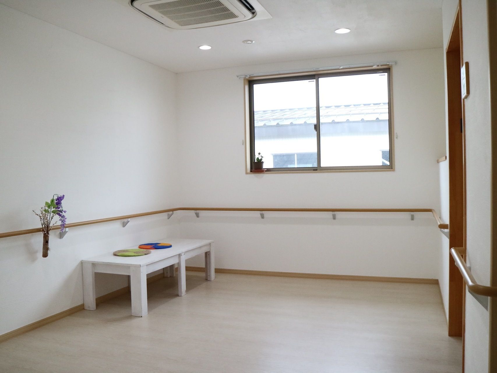 白い壁に手すりや窓が設置され、白いベンチが置かれている休憩スペースである。丸い敷物が2つ並べられている。