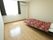 フローリングのワンルームの部屋には、窓があり、カーテンがついている。その横にエアコンが設置してある。右手にベッドが置いてある。