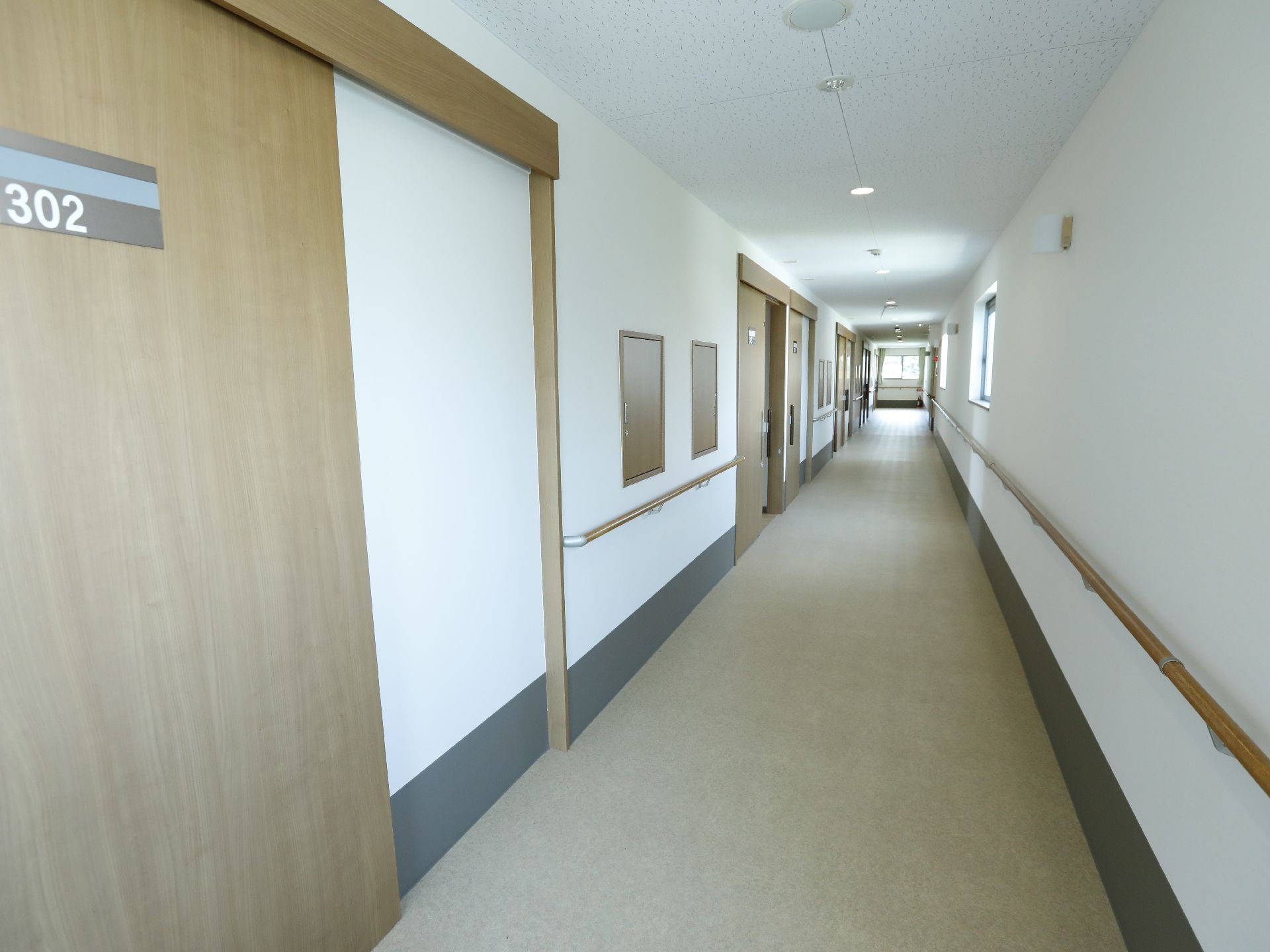 廊下の左右の壁には手すりが設けてある。左手には入居者様用の部屋がある。扉はスライド式なので、簡単に開閉ができる。