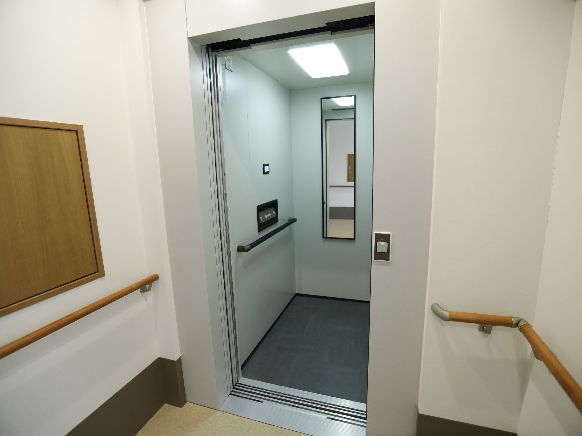 エレベーターが一基あり、扉が開いている。鏡が中にあり、廊下が映っている。内部に手すりがついているので、運行中に掴まることができ安全である。