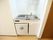 白い壁と茶色のフローリングの部屋で、白い括り付けの棚がシンクの上にある。シンク下にも収納がある。ワンドアの冷蔵庫がある。