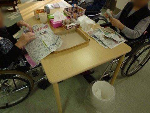 車椅子対応のテーブルで新聞を読む女性と作業されている女性