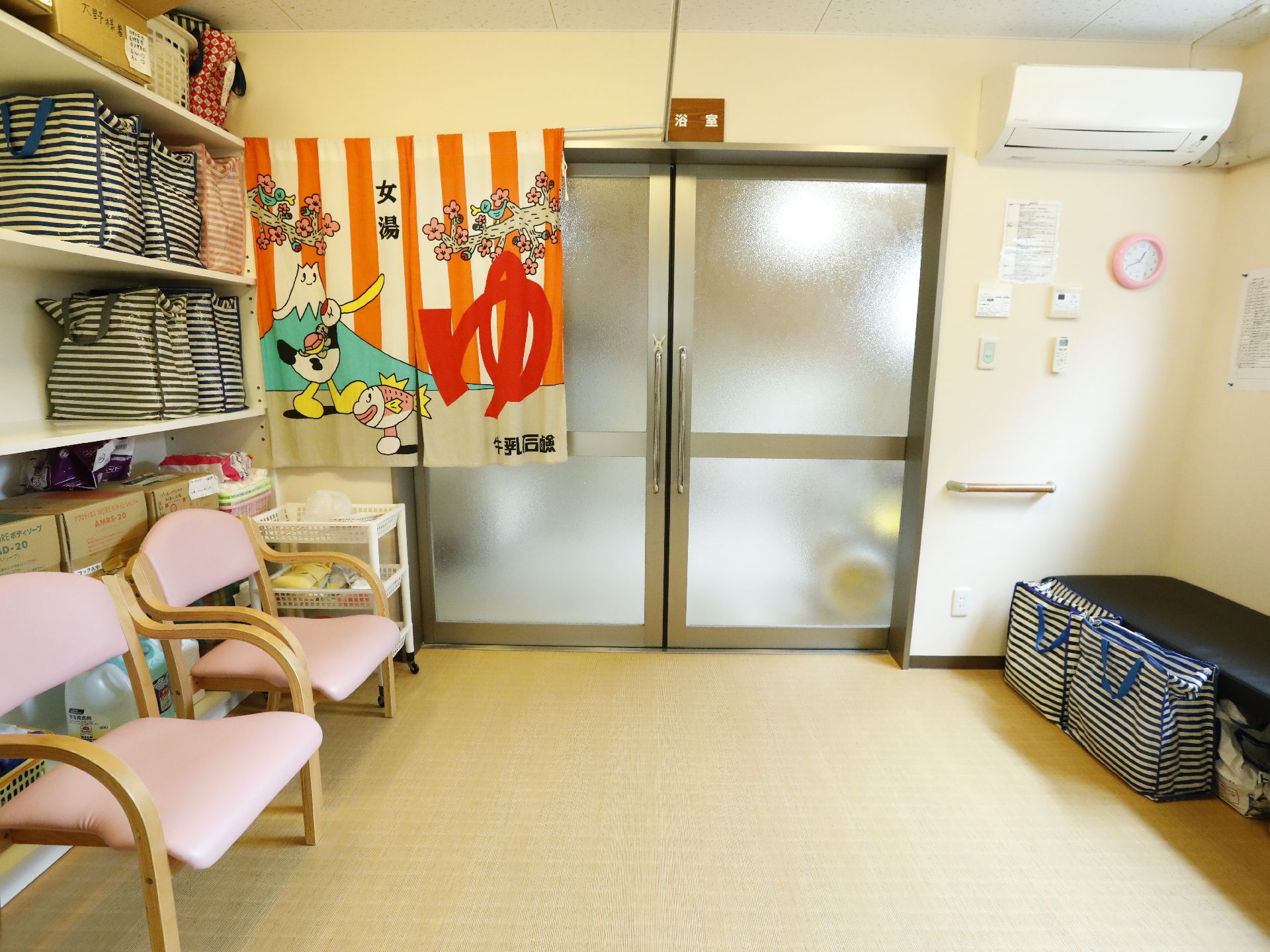 広さのある脱衣所。長椅子と一人用の椅子が用意されている。収納棚や長椅子の下には入浴関係の物品が整頓されている。