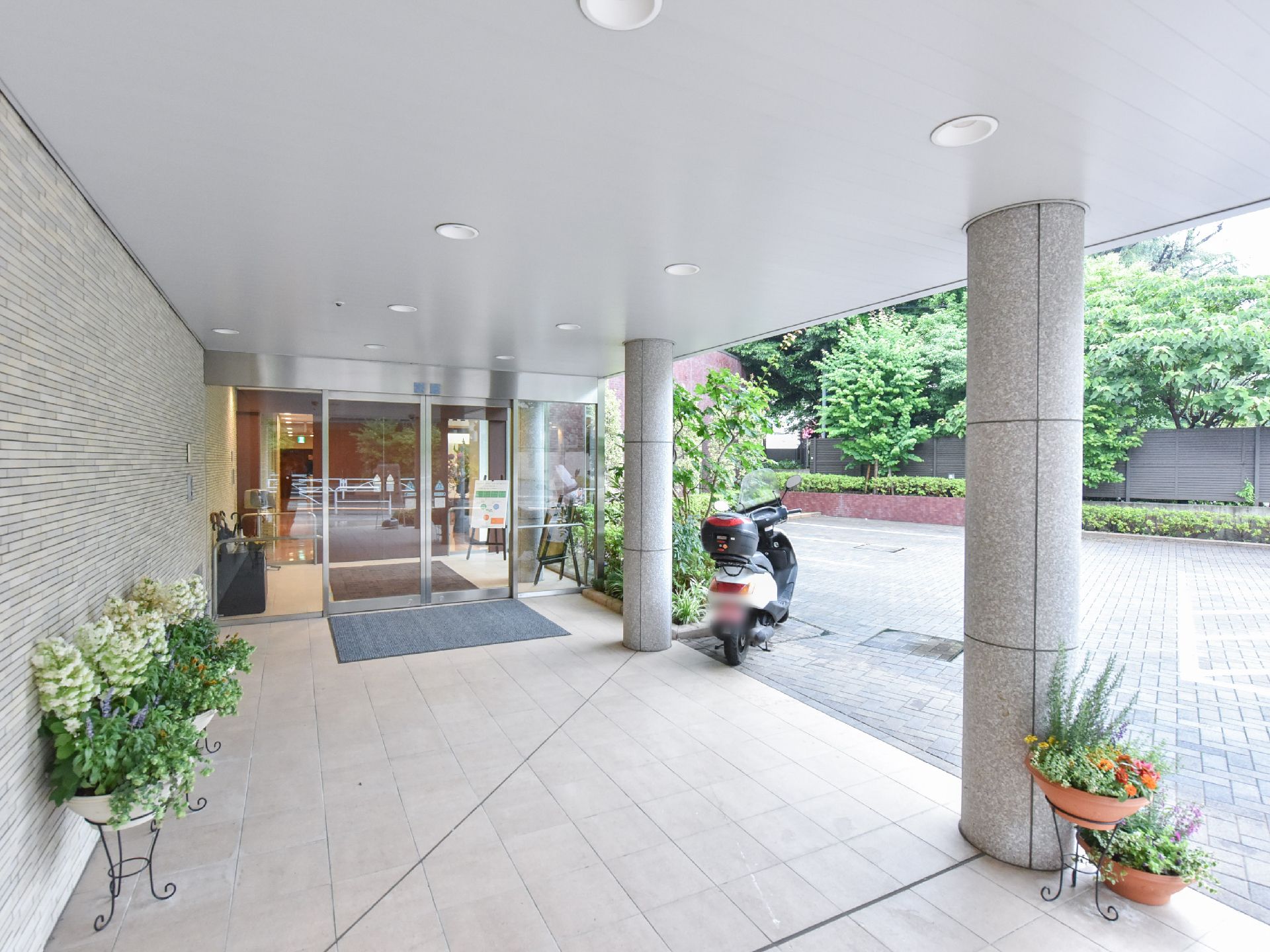 おしゃれな寄せ植えが並ぶアプローチ。車同乗の方はここで降りれば雨の日は濡れずに済む。監視カメラも配置。