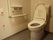落ち着いた色調でまとめた絨毯敷きのトイレ。手すりやストックしておける２つのトイレットペーパーホルダー付き。