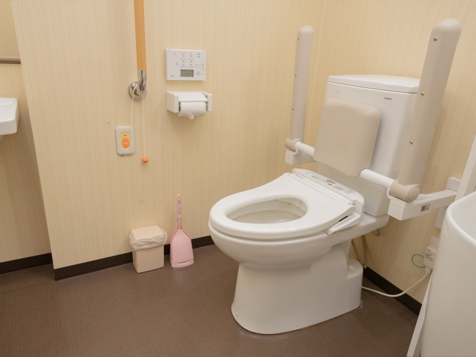ベージュのクロスにブラウンの床が落ち着いた雰囲気のトイレには洗面台、オストメイト対応の流し台も設置された多機能型になっている。