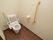 ベージュの壁とフローリングの床が明るい雰囲気の広々としたトイレには手すりや緊急通報装置が設置されている。