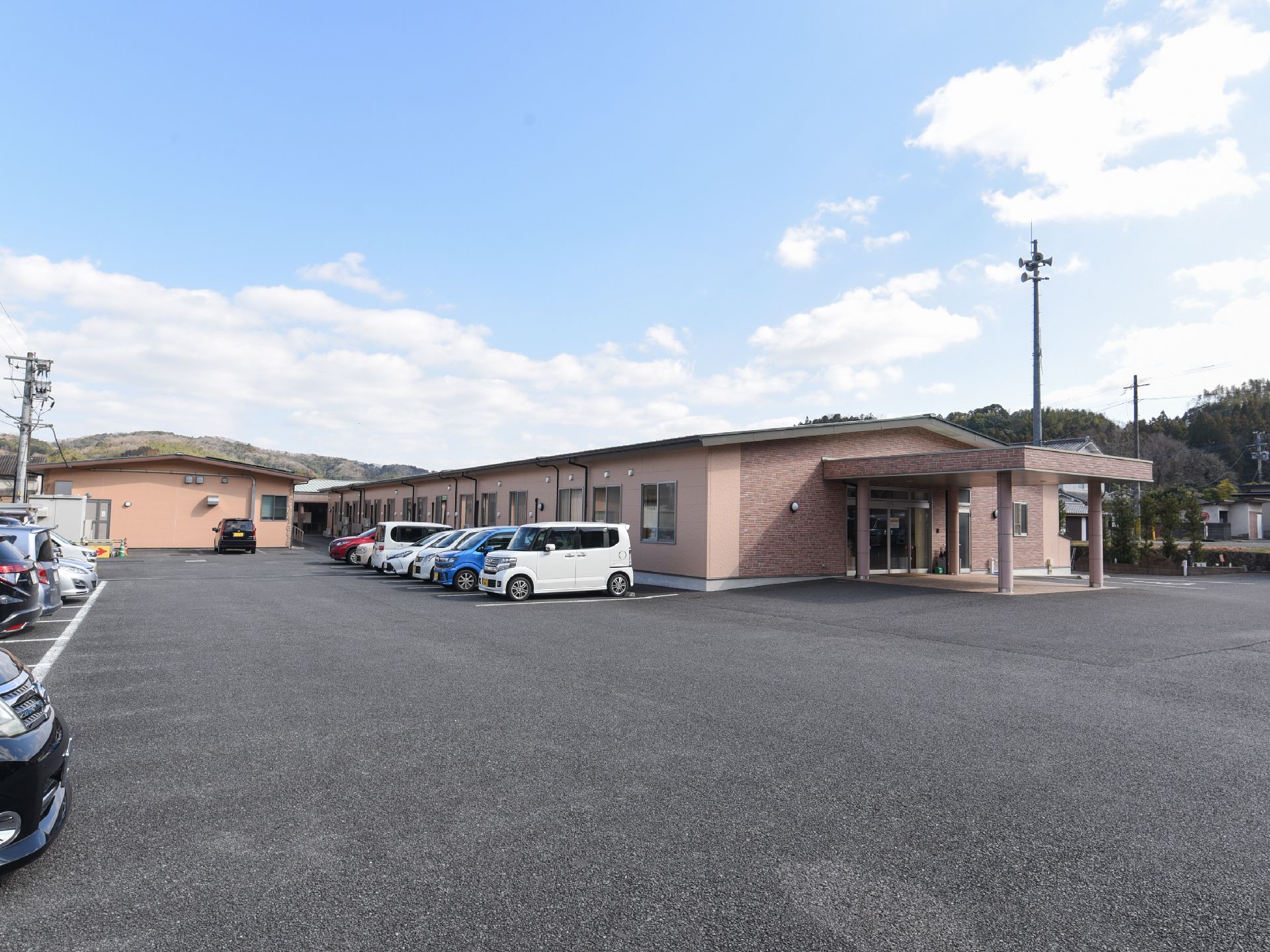 レンガ調と、ピンクベースの平屋造りの施設建物である。駐車スペースは広く、玄関まではフラットに施工されている。