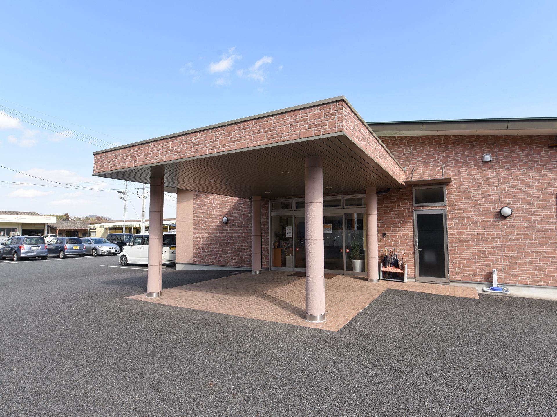 風合いのあるピンク系のレンガが特徴的な建物に、大きくしっかりとした屋根のある玄関ポーチである。段差のないアプローチになっている。