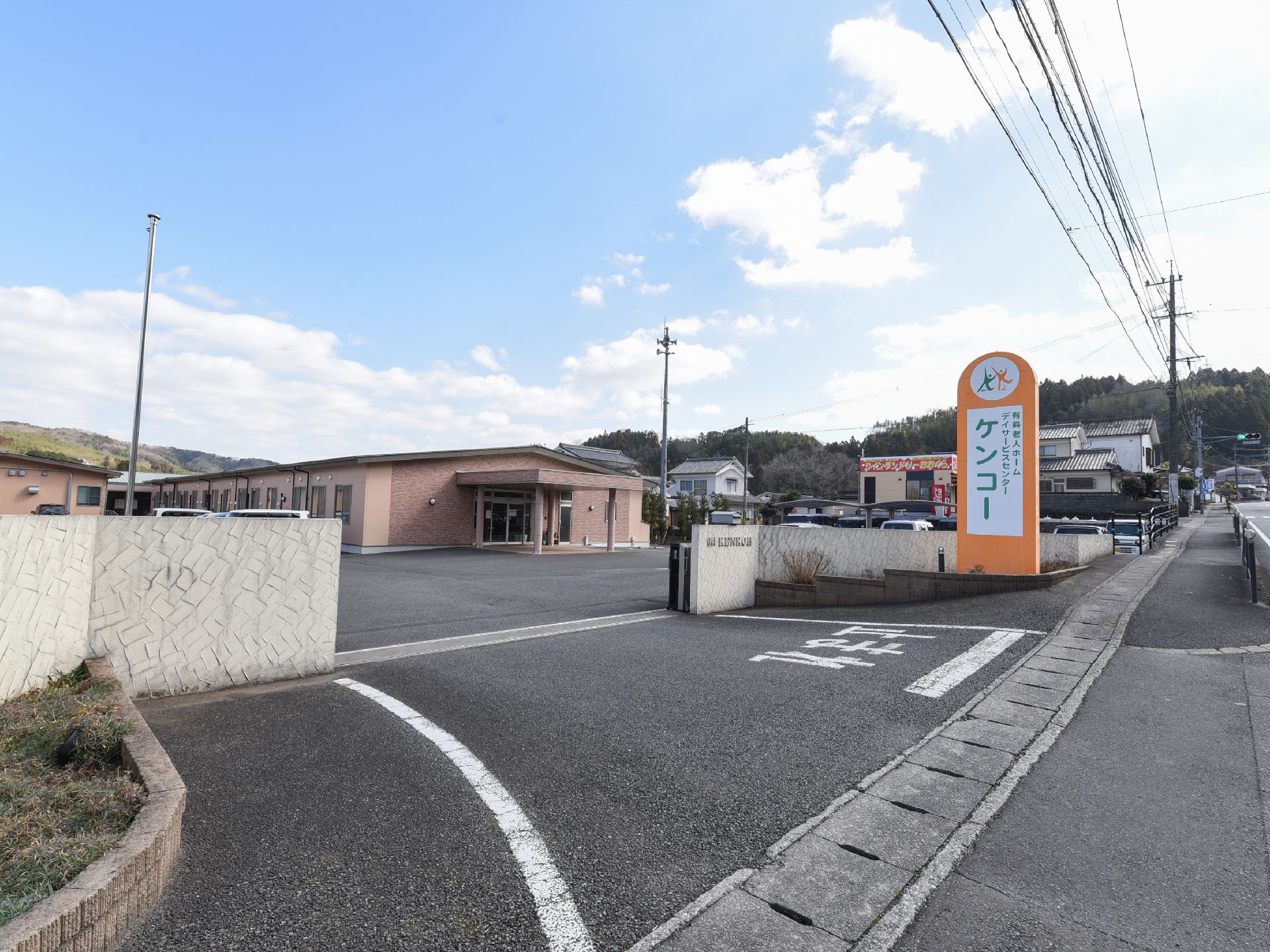 施設敷地への入口は塀と門で境界を造っている。入口付近には、施設名を掲げたオレンジ色の大きな看板を据えている。