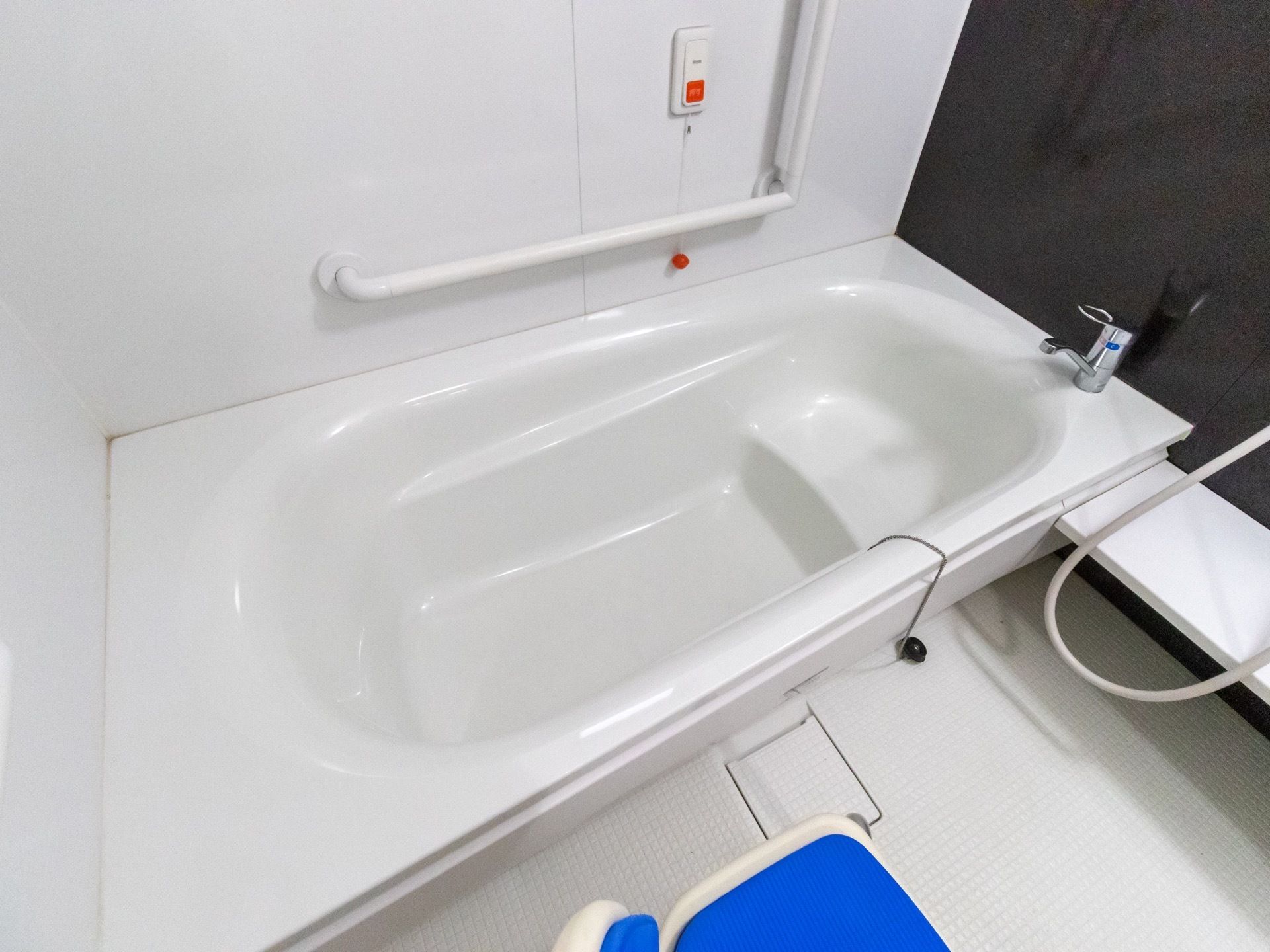 白を基調とした清潔感のある浴室となっている。洗い場には、青色の椅子が１脚置かれ、壁にはナースコールが設置されている。