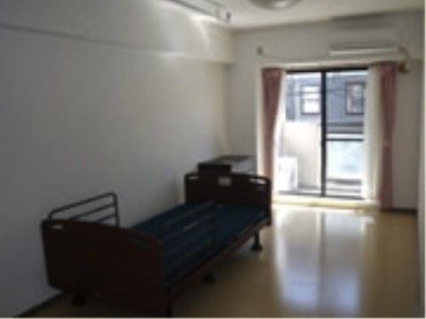 エアコンが設置され、介護用ベッドが置かれたベランダ付きの居室