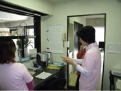 ガラス越しに入口が見える受付の中で話し合いをしている２人のスタッフ