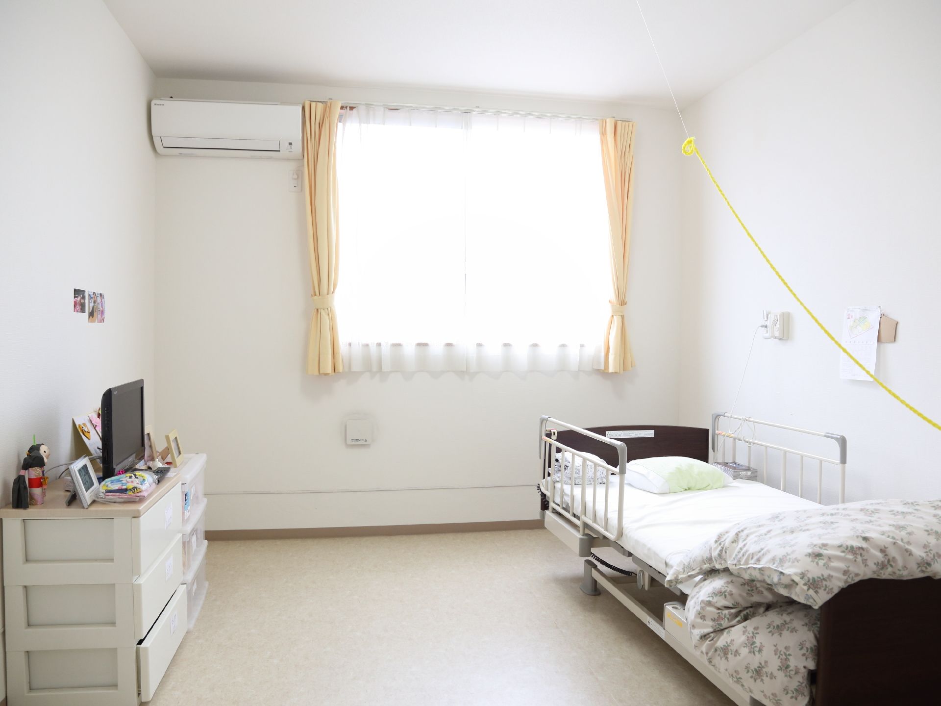 ある居住者の個室写真。奥に窓があり、その前に柵が付いたベッドが置かれている。ベッドの反対側には、洋服ダンスが置かれている。