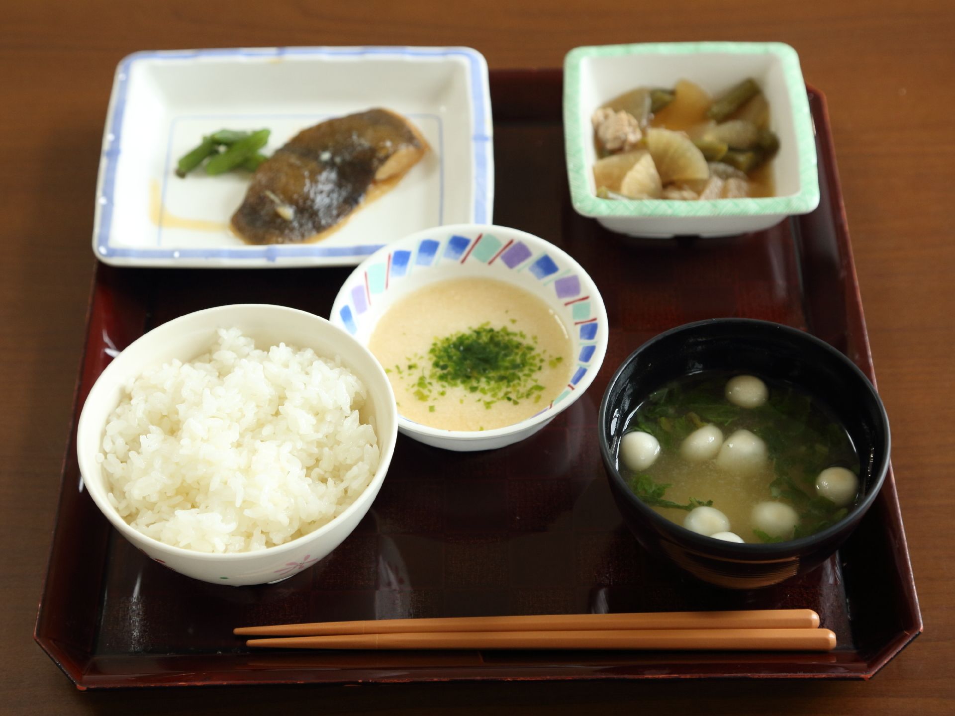 施設で提供される、食事の一例。四角いお盆に、箸と一汁三菜の食事が並んでいる。メインは魚で、野菜のおかずがある。
