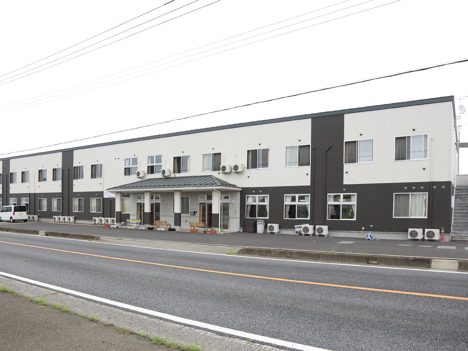 施設は道路に面した場所に建っている。2階建ての建物で、外階段がついている。施設の前に、駐車スペースがある。