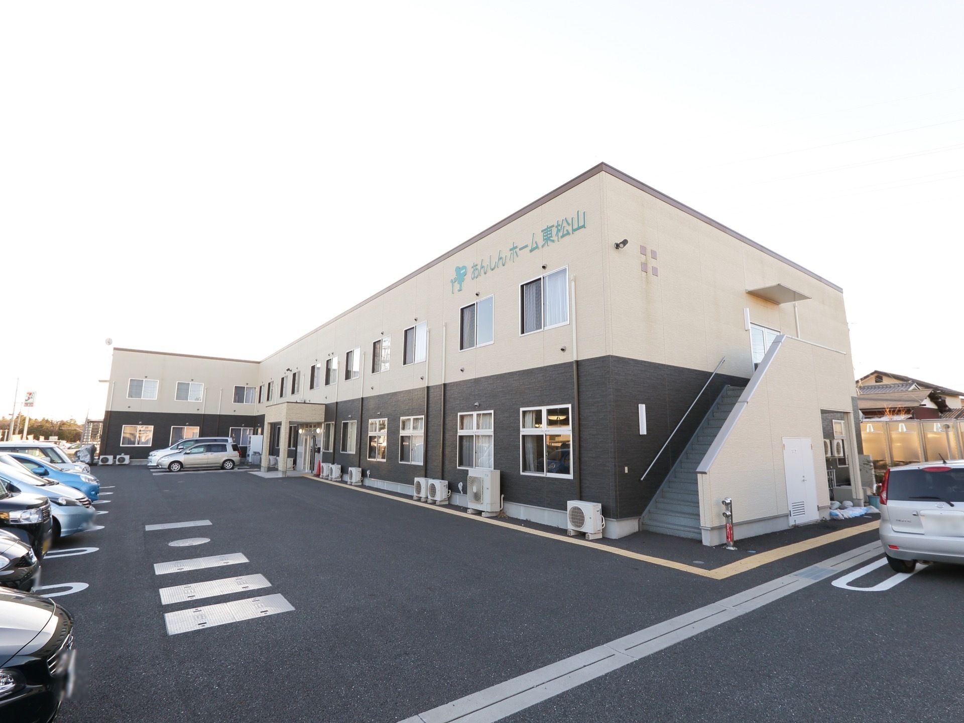広々とした敷地に2階建てで立地して施設の外観。建物の前にはコンクリートで整備された駐車場が設けられている。