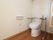 木目調のフローリングのトイレである。便座の両側には手すりを備えている。横側の壁には、ペーパーホルダーとナースコールがある。