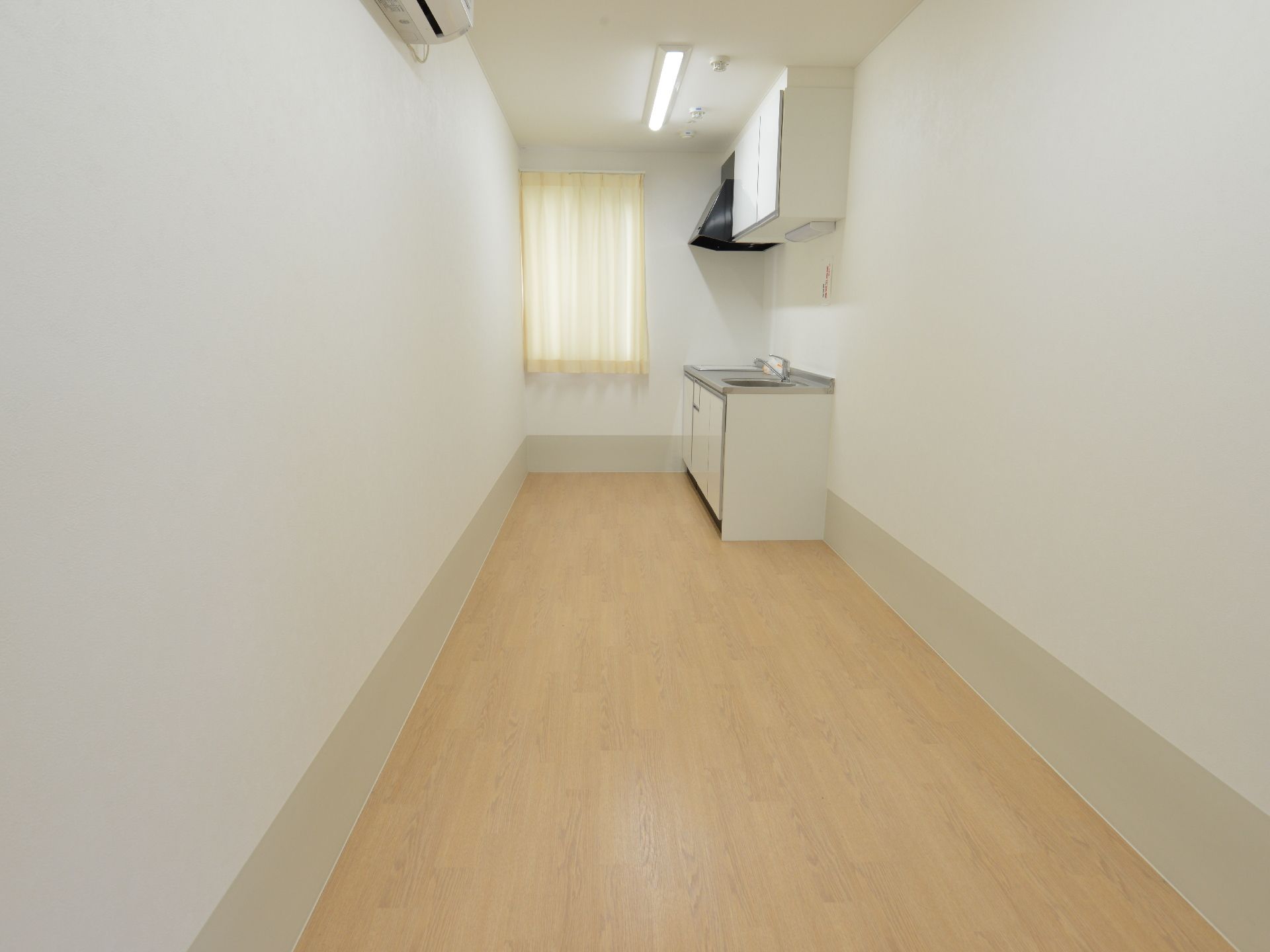 細長い部屋が特徴的である。キッチンが設置されている。エアコンが完備されている。白い壁が清潔感がある。