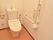 逆L字型の手すりがついているトイレルームは、洗浄機付きの便座があり、非常用ブザーも設置されているのが見える。