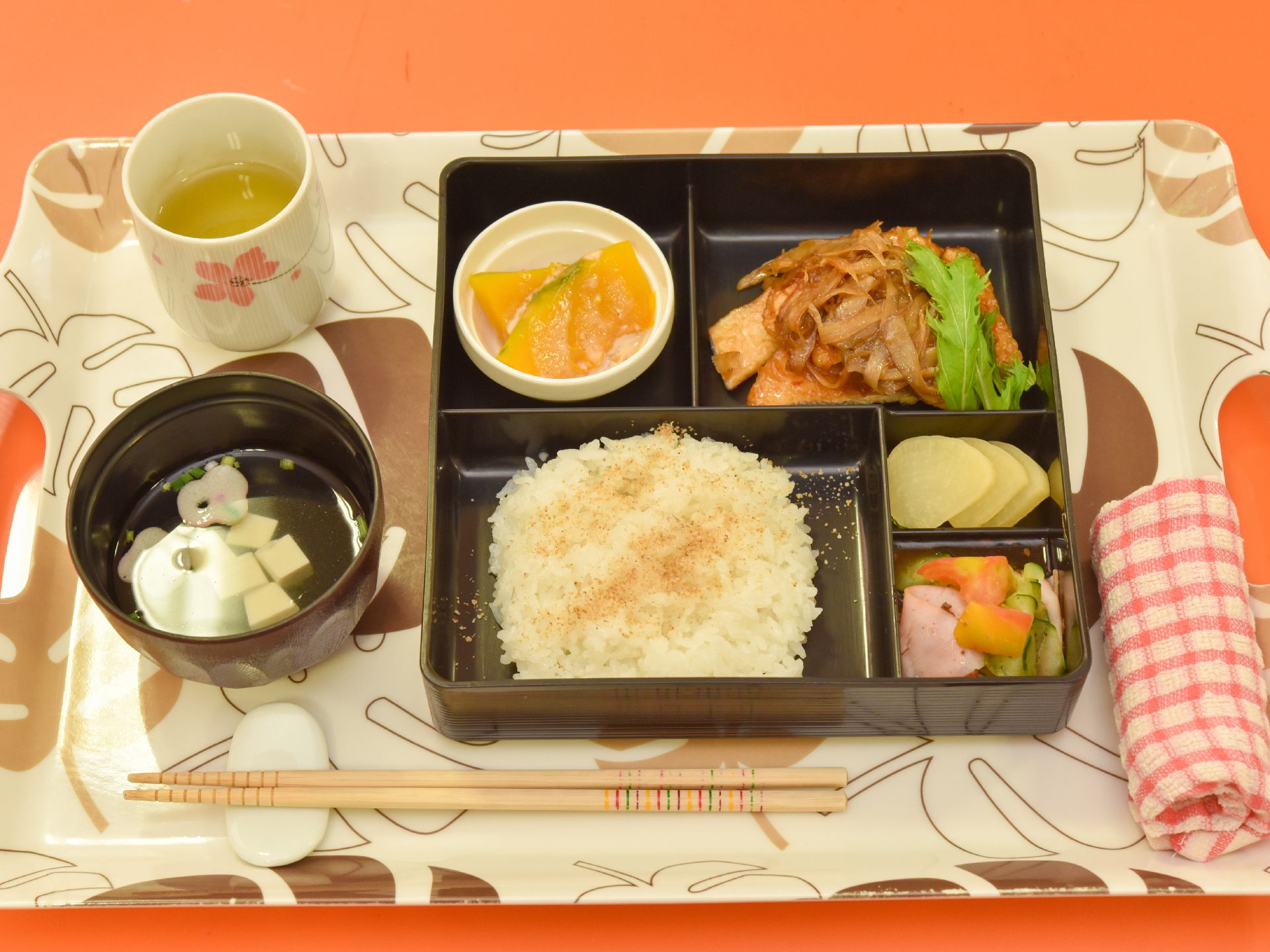 白を基調としたお盆の上には、お弁当のように仕切られたエリアごとにおかずやご飯がのっており、片隅にはお茶やお吸い物もある。