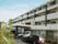 ４階建ての白い外観の建物で、１階の中央付近に玄関があり、大きなひさしが付いている。建物に沿って、駐車スペースになっている。