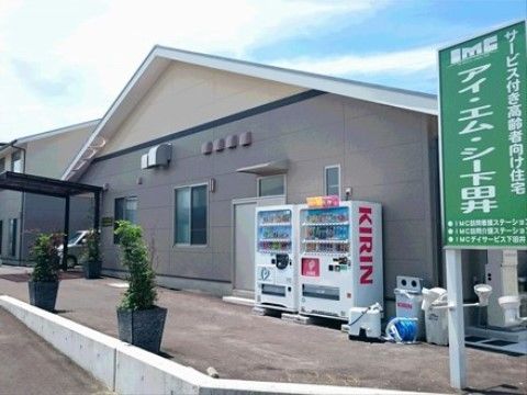 新築の建物は外壁が淡い色調で優しい雰囲気。玄関までは緩やかなスロープが続き、複数台分の駐車スペースがある。